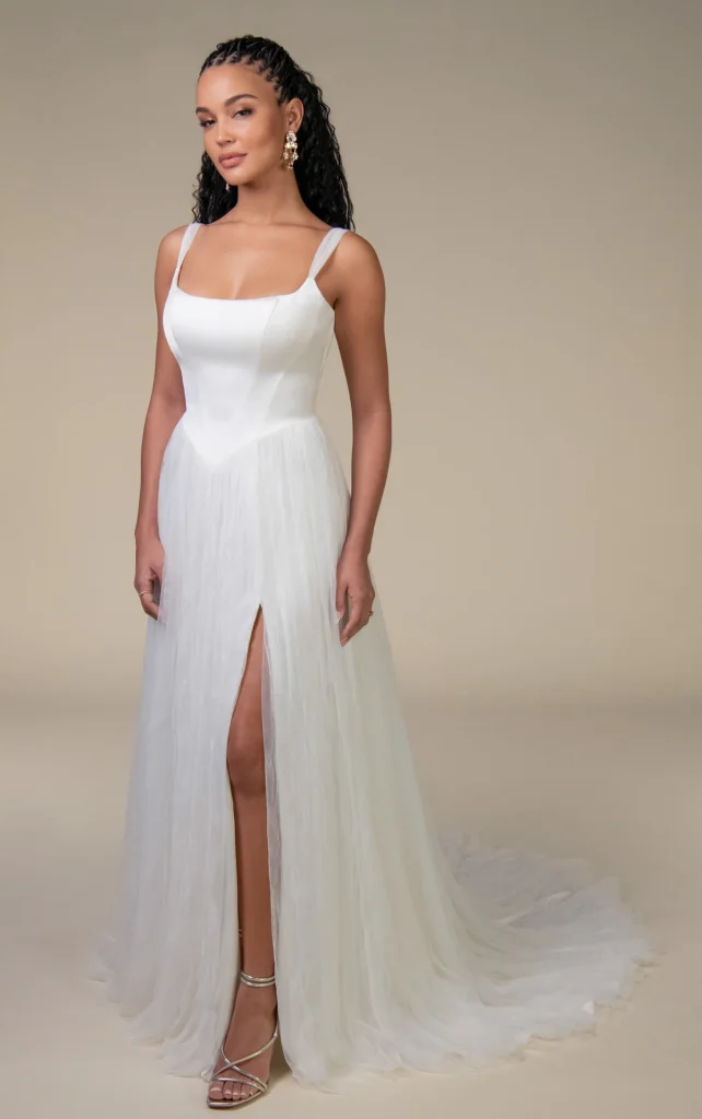 Model wearing the All Who Wander Noah wedding dress with a square neckline, fitted satin bodice, flowing A-line skirt and high slit, available at The Bridal Collection in Denver, Colorado.