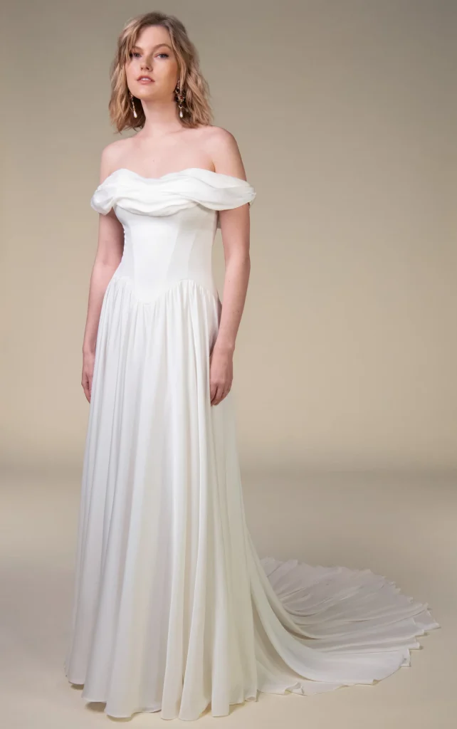 Model wearing the All Who Wander Cosete wedding dress with an off-the-shoulder neckline, draped bodice, basque waist and flowing A-line skirt.