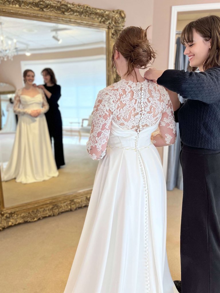 Bride smiling in mirror during a wedding dress fitting appointment.