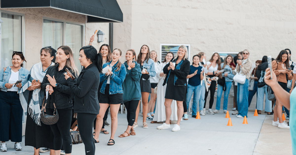 A long line of enthusiastic brides and guests clapping and waiting outside the building entrance during the National Bridal Sale Day at The Bridal Collection.