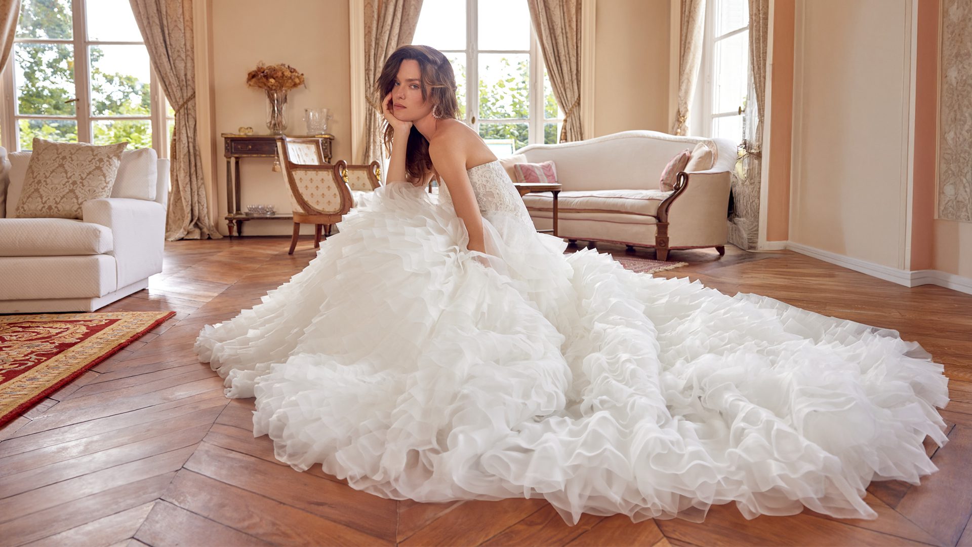 Model wearing the Justin Alexander Magdalena wedding dress with a strapless lace bodice and dramatic ruffled ball gown skirt with a sweeping train, available at The Bridal Collection in Denver, Colorado.