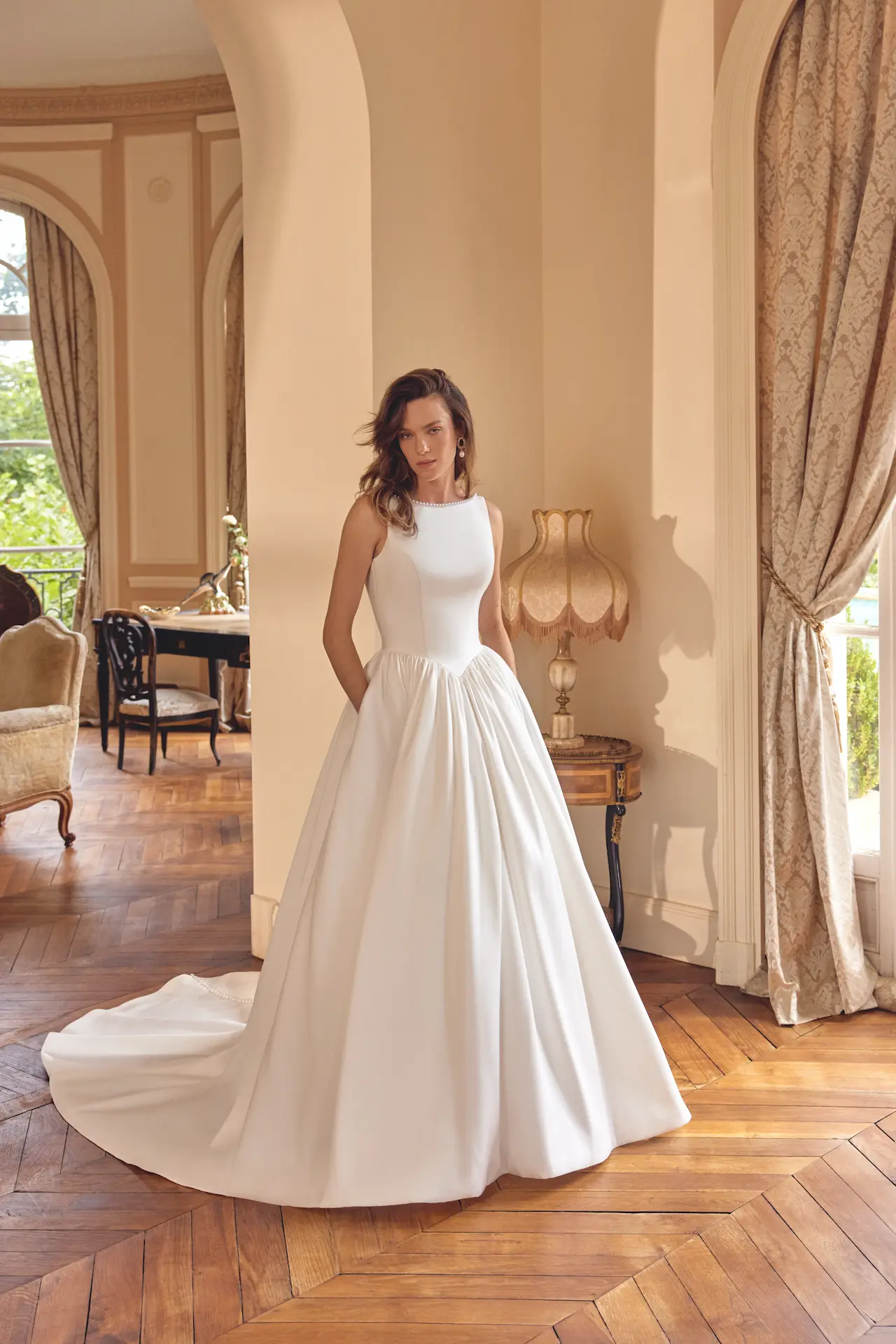 Model wearing the Justin Alexander McKenna wedding dress with a pearl-trimmed high neckline, basque waist and full Mikado ball gown skirt with a sweeping train.